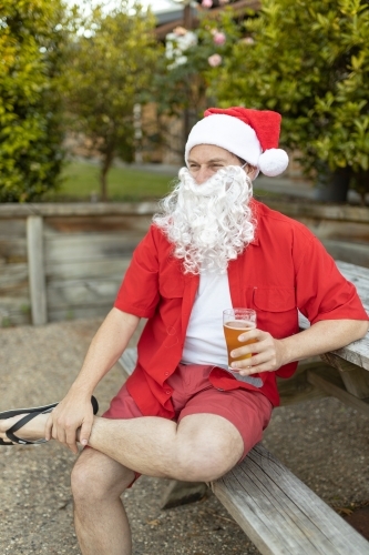A Santa Claus at Christmas time in  the Australian summer holding a beer
