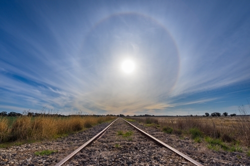 A solar halo low in the sky over receding railway tracks