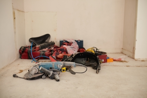 A tradesmans tools on the ground in the corner of a room