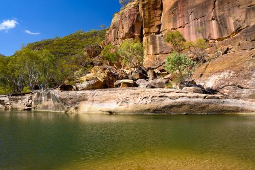 A waterhole in a gorge with orange sandstone rock formation and blue sky