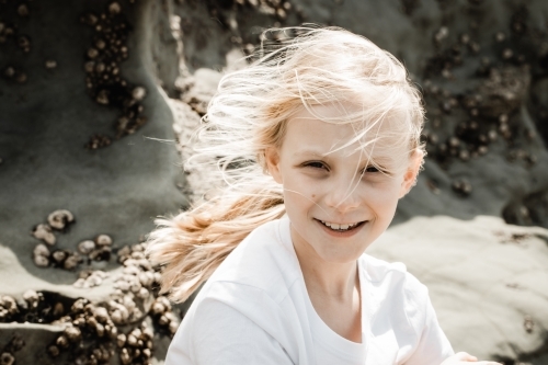 A young girl sitting at a beach cliff with wind blown hair