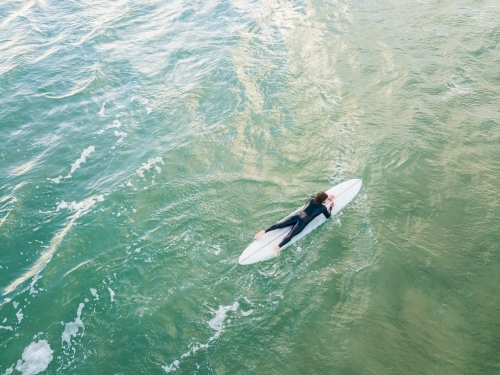 Aerial view of a lone surfer paddling a board on the ocean