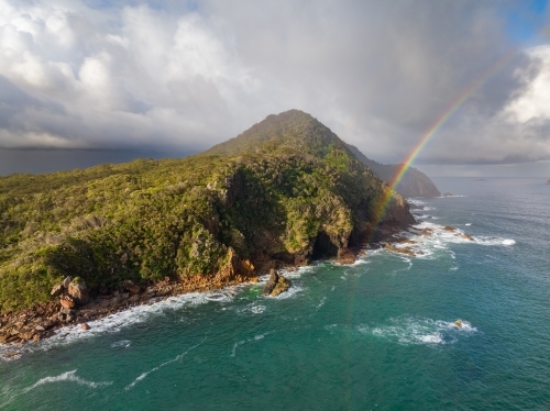 Aerial view of a rainbow over a coastal headland with dramatic clouds above