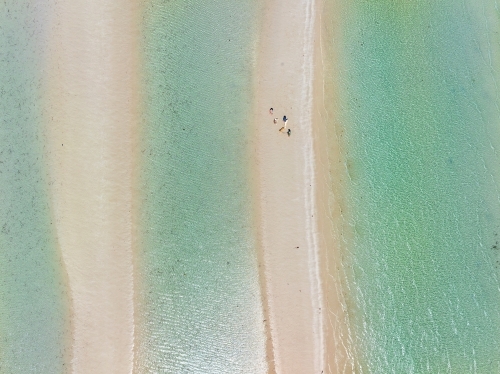 Aerial view of people walking on a narrow sandy  beach between pools of clear water