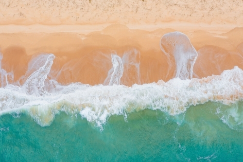 Aerial view of wave crashing and leaving patterns on a wide sandy beach