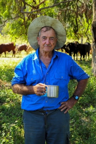 An old farmer enjoying his morning cup of tea in the shade of trees.