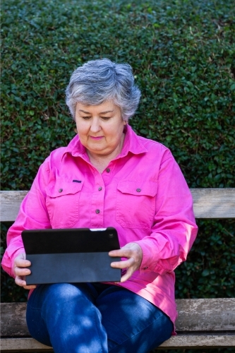 An old lady sitting on the bench using her tablet