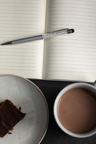 an open notebook with a mug of hot chocolate and piece of chocolate brownie