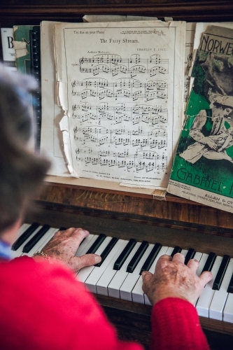 Anonymous old lady playing the piano with sheet music, wearing a red cardigan