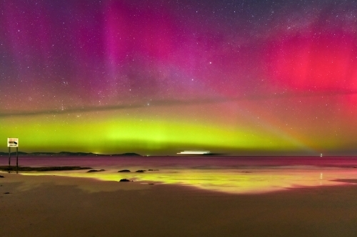 Aurora Australia illuminating the night sky and reflecting on a wet sandy beach