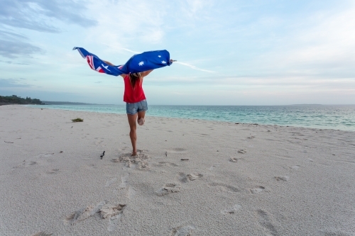 Australia Day - a woman leaps into the air with the Australian Flag above her head on a beach