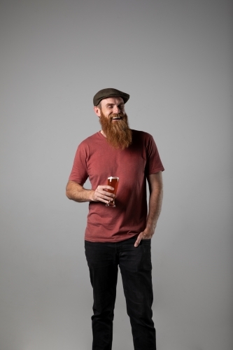 Bearded man in tweed flat cap standing holding a beer.
