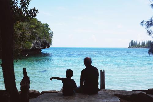 Boy and grandpa looking at ocean from behind