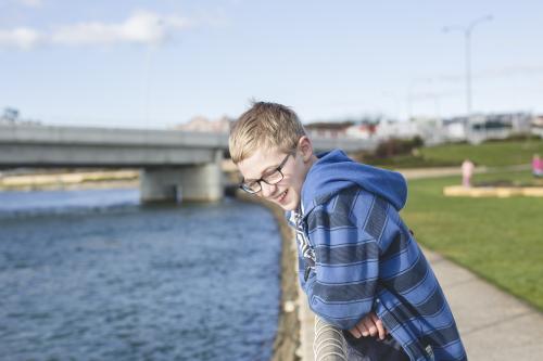 Boy leaning over fence near river