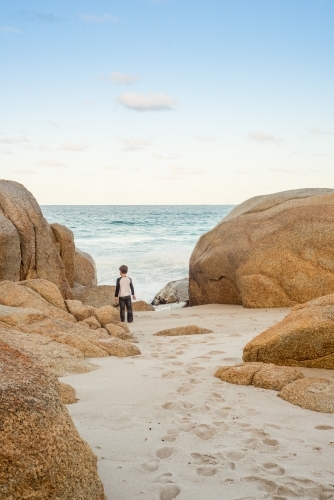 Boy on sandy beach surrounded by boulder rocks