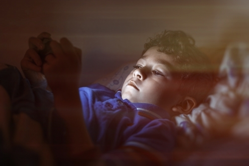 Boy using smart phone in dark bedroom