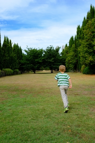 Boy walking into a large green field with trees