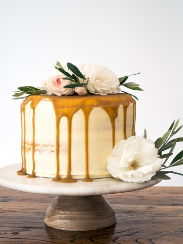 Caramel drip layer cake on cakestand with flowers
