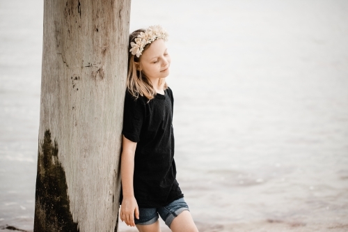 Caucasian girl standing underneath a pier at the beach wearing a flower head band
