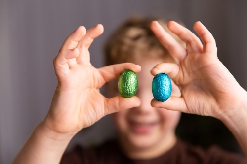 child holding up Easter eggs between fingers