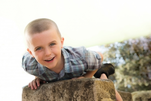 Child smiling at camera while laying on rock at park.