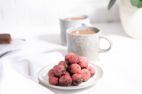 Chocolate protein balls on a white kitchen bench with two mugs