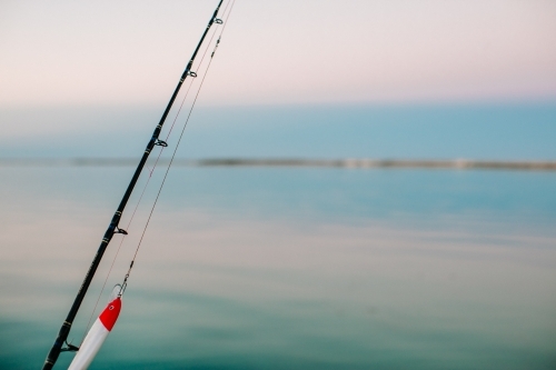 Close-up of a fishing rod with lure with a calm ocean and sky in the background