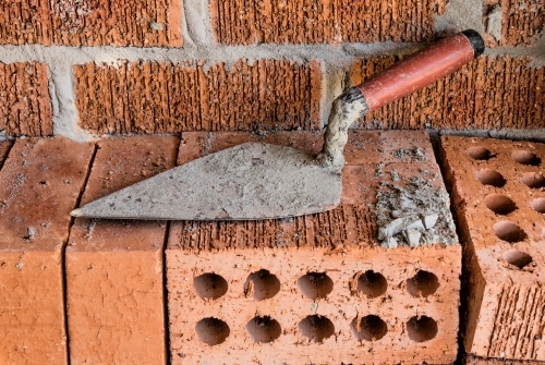 Close-up of rugged brick wall with loose bricks & trowel on building site