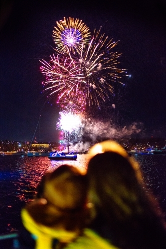 Colourful fireworks display over water with out of focus people in foreground