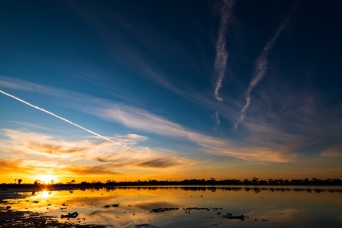 Colourful sunset over a lake with jet streams and reflections