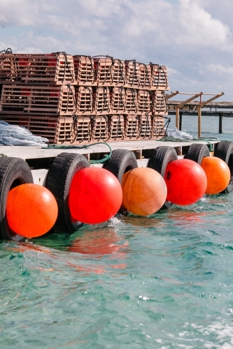 Commercial crayfishing with stacks of craypots and big orange buoys along the wooden jetty