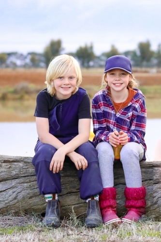 Country kids sitting on log on farm with dam in background