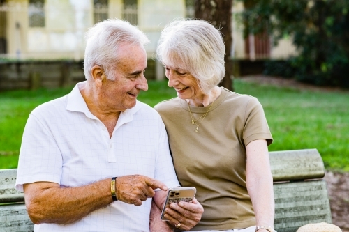 couple sitting on park bench, using phone