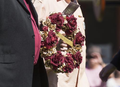 Detail of two people carrying a wreath with red and gold flowers on ANZAC Day