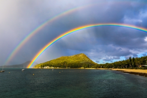Double rainbow over mountain and ocean against cloudy sky