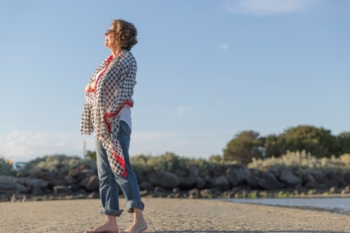 Elderly middle eastern woman standing on beach