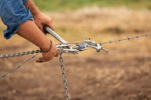 Farmer's hands working a wire strainer while fencing