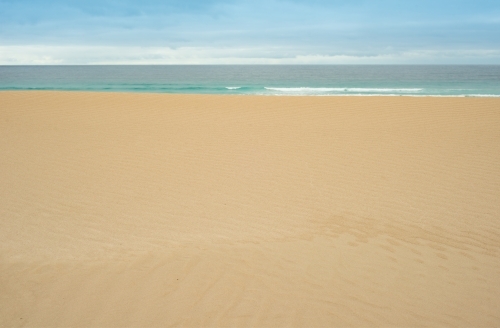 Flat, untouched sand leading to calm ocean in the background