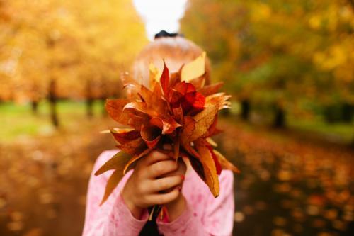 Girl holding Autumn leaves up to her face