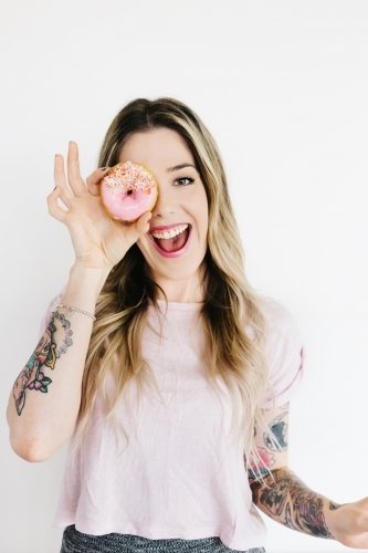 Girl laughing and holding a pink iced donut to her face to look through the hole