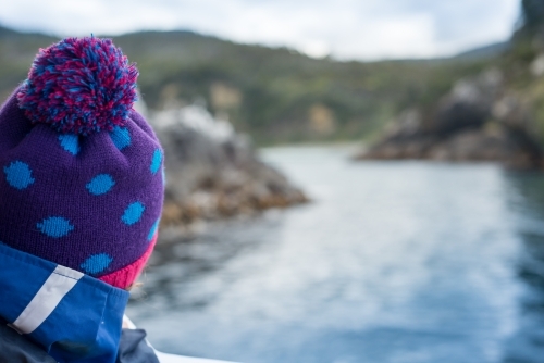 Girl looking at ocean water and rocky land from boat on a cold winter day