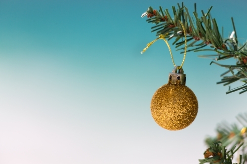 Gold glitter bauble on Christmas tree with beautiful beach background blur.