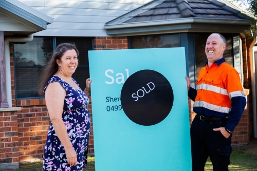 Happy middle aged couple smiling with newly purchased house sold sign