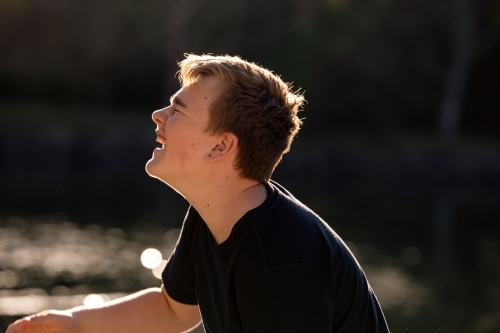 Happy teenage boy by the water in golden afternoon sunshine