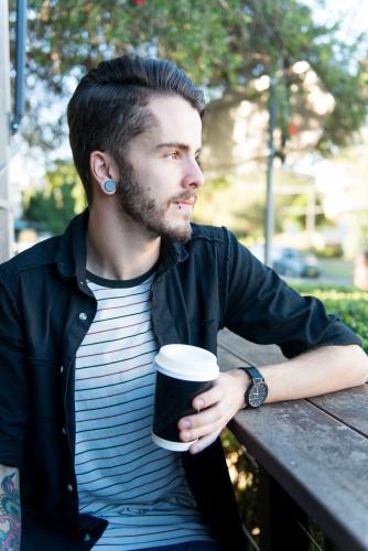 Hipster man sitting outdoors with a take away coffee
