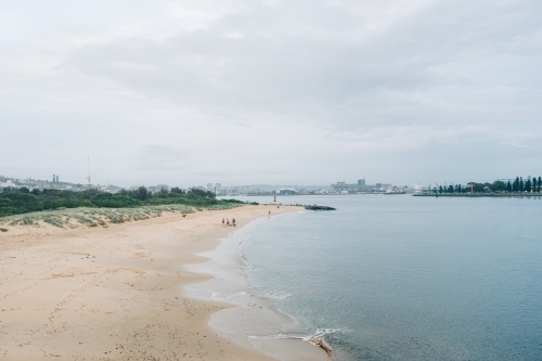 horizontal shot of a beach front with white sand, trees, buildings and people on a gloomy day