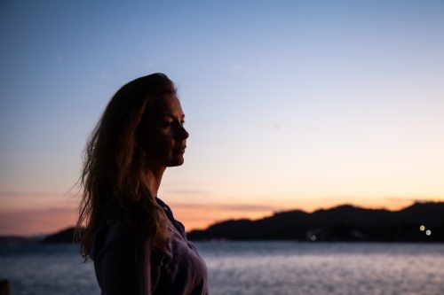 horizontal shot of a silhouette of a woman by the beach with mountains and sunset in the background