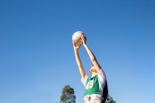 horizontal shot of a young woman holding a ball up high in the air on a sunny day with clear skies