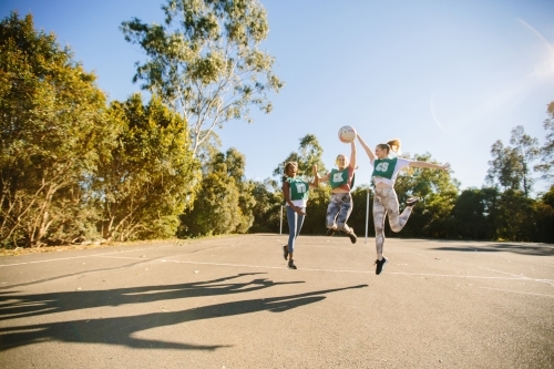 horizontal shot of three young women jumping in mid air on a sunny day with trees in the background