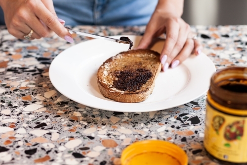 horizontal shot of woman making vegemite toast on a table with color design